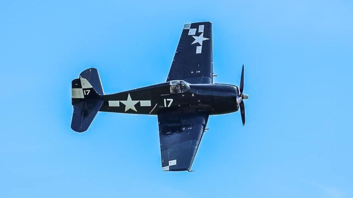 Dark blue Grumman F6F-5N Hellcat World War II fighter aircraft from the Erickson Aircraft Collection flying overhead, displaying U.S. Navy star insignia and tail number markings against a clear blue sky.
